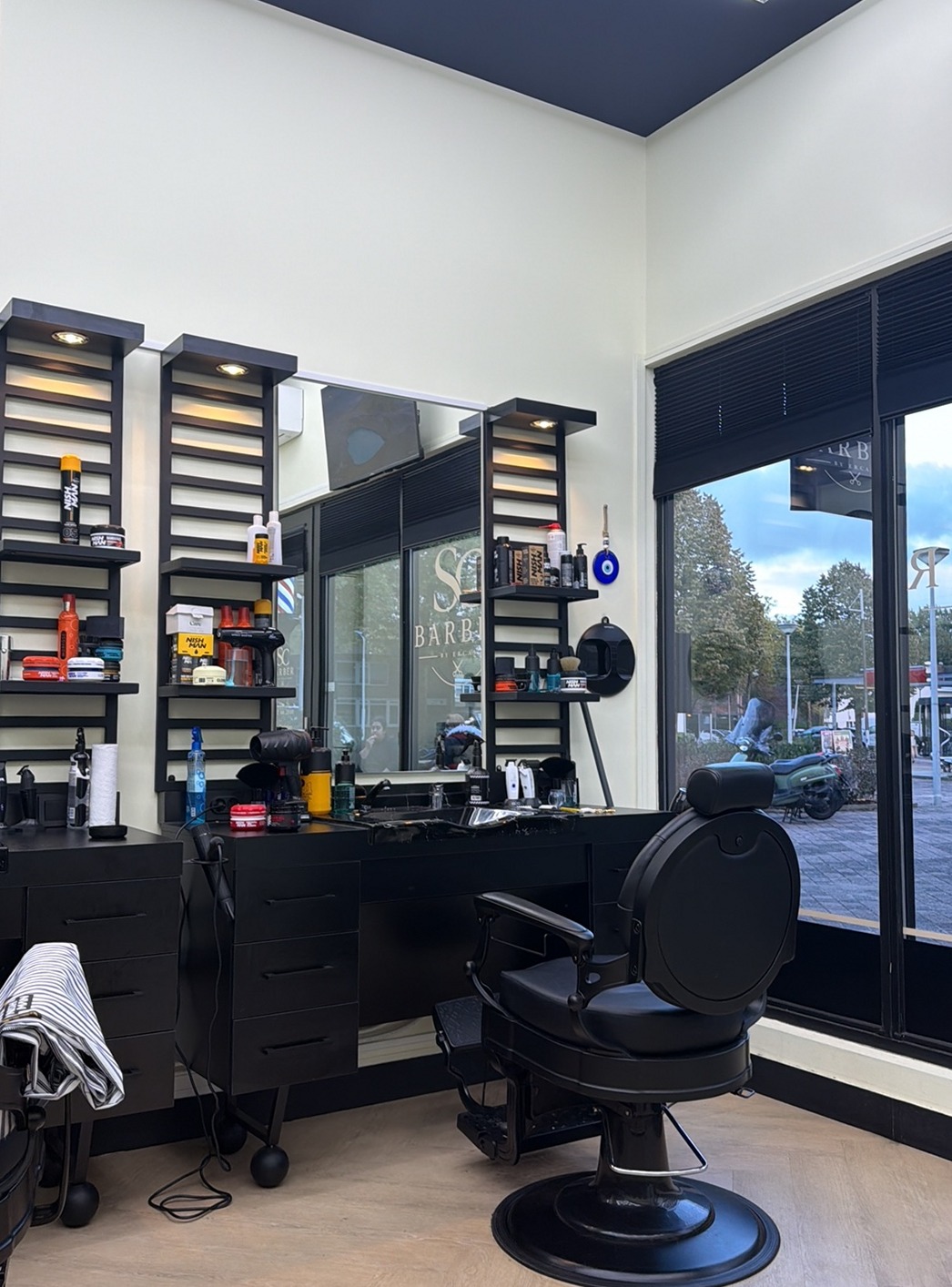 Een werkplek bij SC Barber met zwarte kast, spiegel en kappersstoel bij het raam